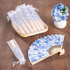 a blue and white fan next to a vase with flowers in it on a wooden table