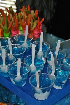 there are many cups and spoons with blue liquid in them on the tray next to carrot sticks