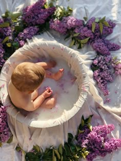 a baby in a bath surrounded by purple flowers