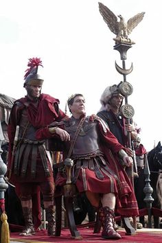 three men dressed in roman costumes standing next to each other on a red carpeted area