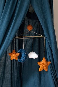 a blue curtain with three crocheted stars hanging from it's sides and two moon mobiles attached to the rod