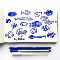 an open notebook with fish drawn on it next to two pens and a bookmark