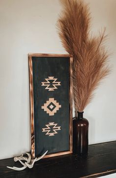 a brown vase sitting next to a black and gold framed painting on top of a wooden shelf