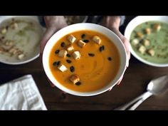 two bowls of soup with croutons and tofu on the side, one being held up by someone's hands