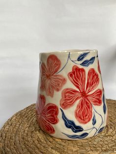 a red and blue flowered vase sitting on top of a straw hat