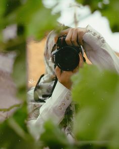 a person holding a camera up to their face in front of some trees and leaves