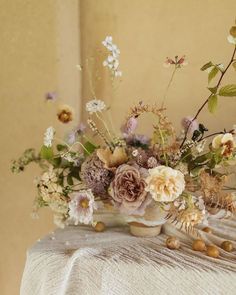 a vase filled with lots of flowers sitting on top of a white cloth covered table