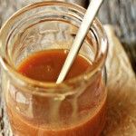 a glass jar filled with sauce sitting on top of a wooden table next to a spoon