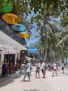 many people are walking on the beach with umbrellas