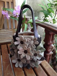 a purse sitting on top of a wooden bench next to a flower pot filled with flowers