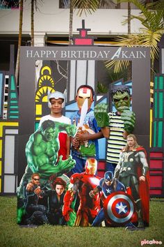 two men standing in front of a sign with avengers characters on it and the caption happy birthday, captain america