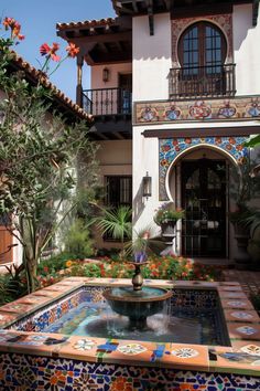 a fountain in the middle of a courtyard with flowers and plants on it's sides