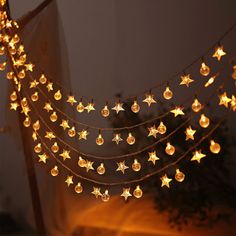 a string of gold stars is hanging from a wire with lights on it in front of a tree