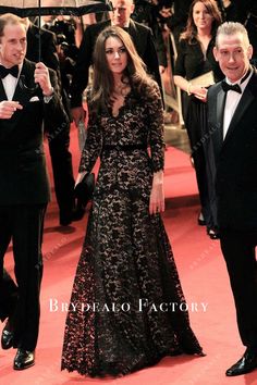 a woman in a long black dress standing next to a man with an umbrella on a red carpet