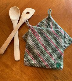 two wooden spoons and a knitted dishcloth on a table with a wood spoon