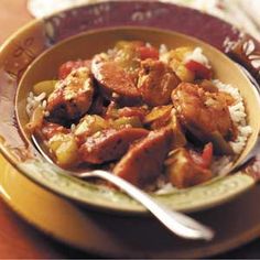 a yellow bowl filled with meat and rice on top of a wooden table next to a fork