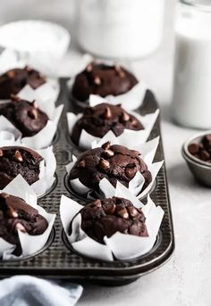 chocolate cupcakes with white paper wrappers on a baking tray next to a glass of milk