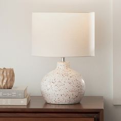 a white vase sitting on top of a wooden table next to a book and lamp