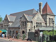 an old stone building with people standing in front and on the side walk near it