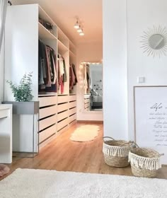 a bedroom with white walls and wooden flooring next to a closet filled with clothes