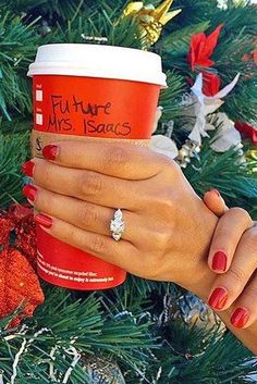 a woman's hand holding a cup of coffee in front of a christmas tree