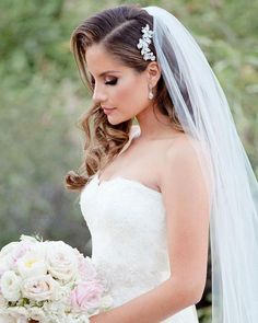 a woman in a wedding dress holding a bouquet and looking down at her hand while wearing a veil