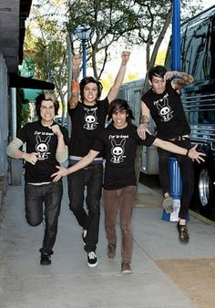 four young men in black t - shirts are posing for a photo on the sidewalk