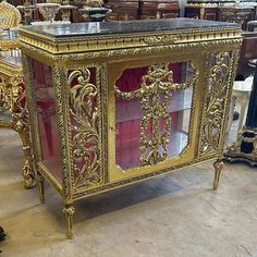 an ornate gold and red cabinet with glass doors in a room filled with other antique furniture