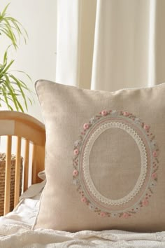 a decorative pillow on a bed in front of a window with curtains and a potted plant