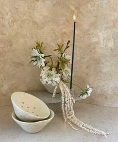 two white bowls with flowers in them next to a candle and some candlesticks