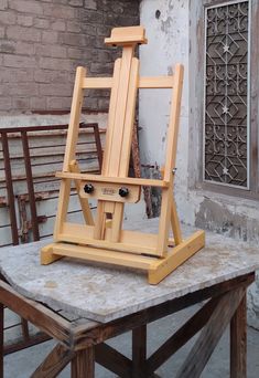 a wooden easel sitting on top of a table next to a brick wall and window