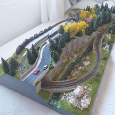 a model train set is displayed on a table with trees and rocks in the foreground