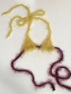 a piece of yellow and purple yarn on a white surface with the thread still attached to it