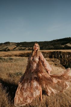 a woman in a long dress is standing in the middle of a field with her hands on her hips