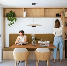 two women sitting at a table with books in front of them and plants on the wall