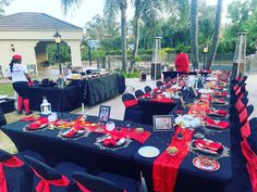 a long table is set up with red and black linens for an outdoor event