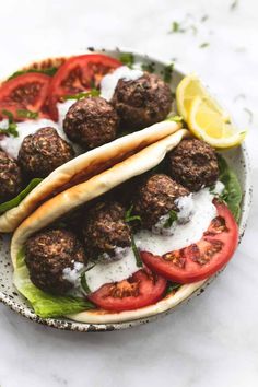 meatballs and pita bread on a plate with tomatoes, lettuce and lemon wedges