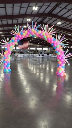 an arch made out of balloons and streamers in a large room with tables set up for a party