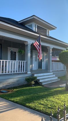 an american flag is on the front porch of a gray house with white railings