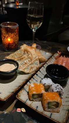 sushi and wine on a table in a dimly lit room with candles, plates and glasses