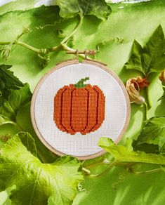 a cross - stitch pumpkin with leaves surrounding it