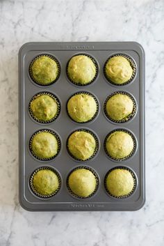 a muffin tin filled with yellow cupcakes on top of a marble counter