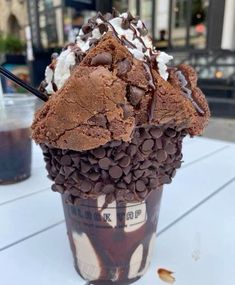 an ice cream sundae with chocolate chips and whipped cream in a plastic cup on a table