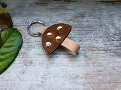 a brown leather keychain with three gold studs on it sitting next to a green leaf