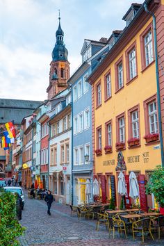 a cobblestone street lined with colorful buildings and tables in front of a clock tower