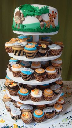 a tiered cake with cupcakes on the bottom and jungle animals on top