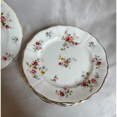 two white plates with flowers on them sitting next to each other in front of a white table cloth