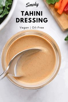 a spoon in a jar filled with tahini dressing next to a cutting board and vegetables