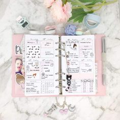 an open planner with flowers and other things on it next to a pink flower pot