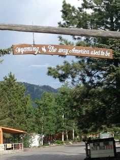 a sign hanging from the side of a wooden pole over a street next to a forest